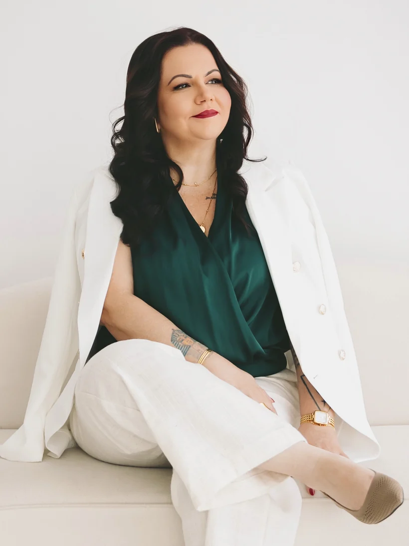 Daniela Lefebvre sentada em um sofá, de blazer branco e blusa verde